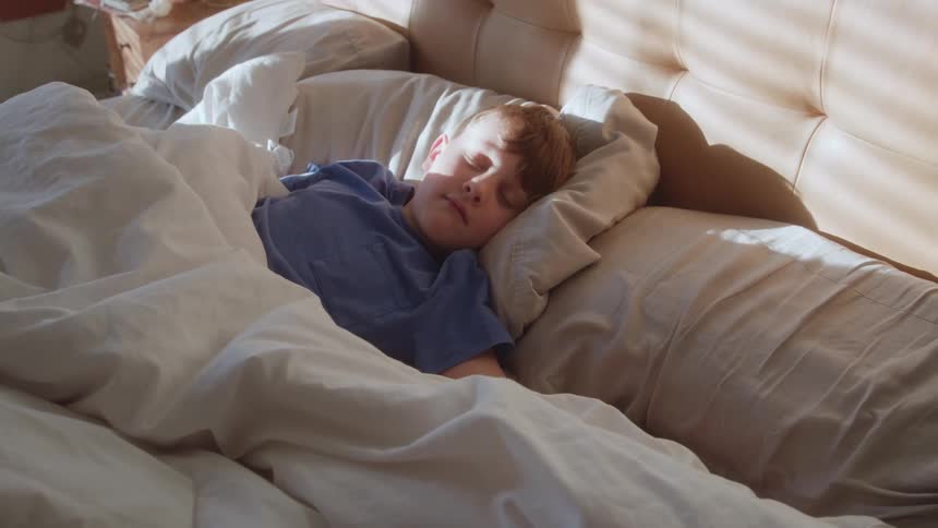 A young boy is asleep while covered by a comforter in a large bed