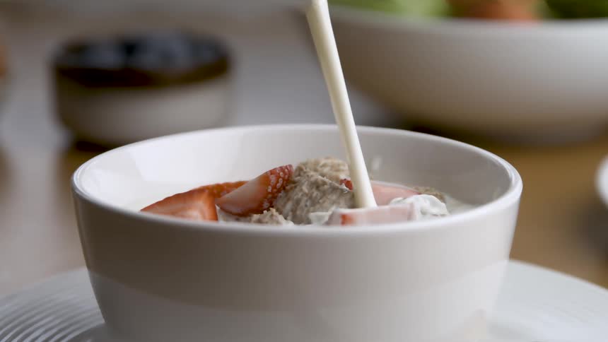 Closeup of cream being poured into a bowl of cereal with strawberries