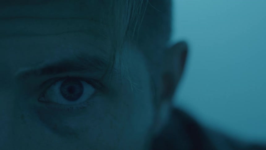 This is an extreme closeup shot of a persons eye and forehead illuminated by an intense cold blue light on their left side the person looks offcamera with a serious or intense expression while the strong blue light creates a dramatic