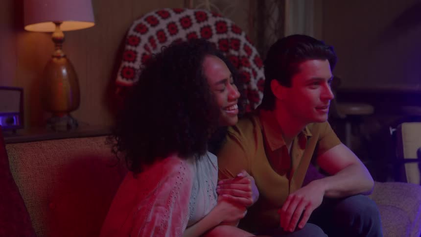A couple is watching a horror movie on tv while sitting on a sofa in their livingroom