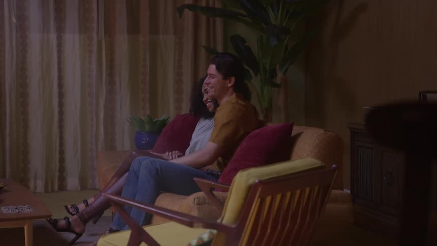 A smiling couple relaxing on a vintage couch in a dimly lit living room