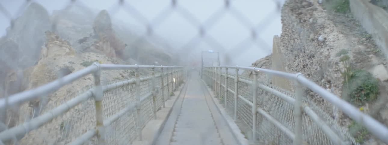 Looking through a chain link fence at a narrow foot bridge
