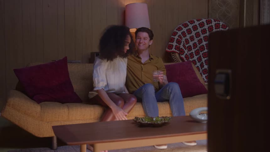 Smiling couple sits on a couch watching tv in a dimly lit living room