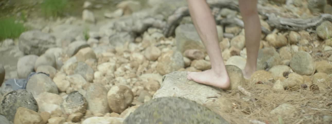 A barefoot man walks over the rocky ground