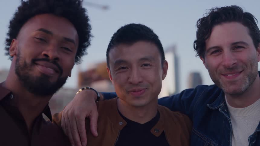 Three men smiling with arms around each other outdoors