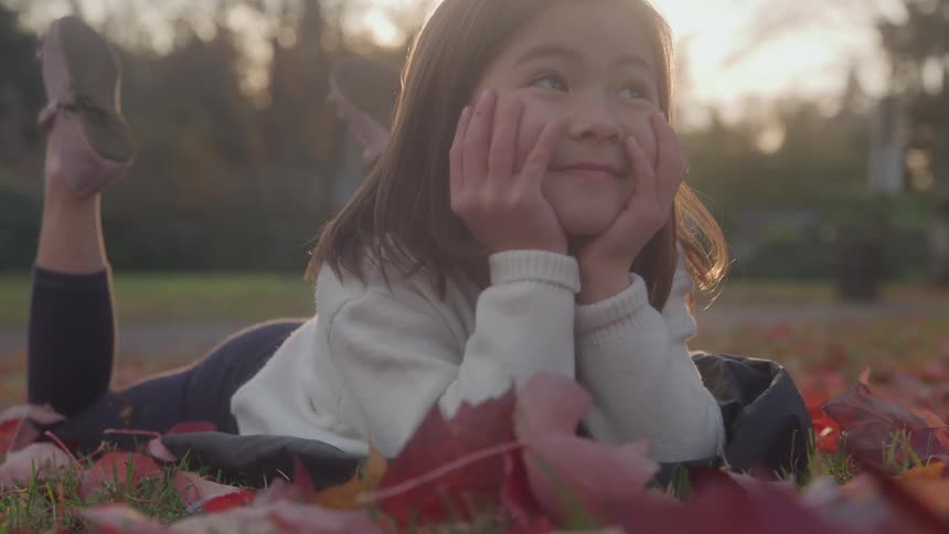 Young asian girl lying on autumn leaves in a park at sunset