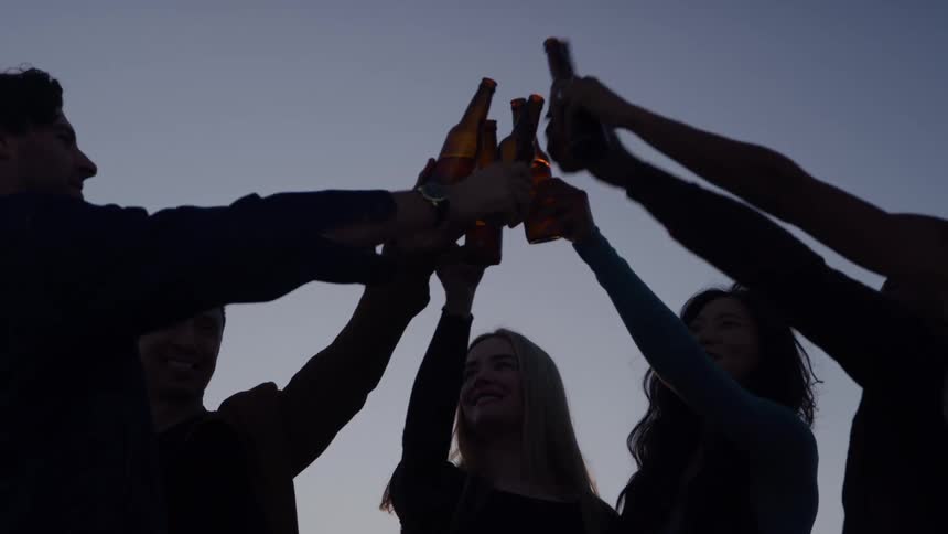 Group of friends clinking bottles in celebration at dusk