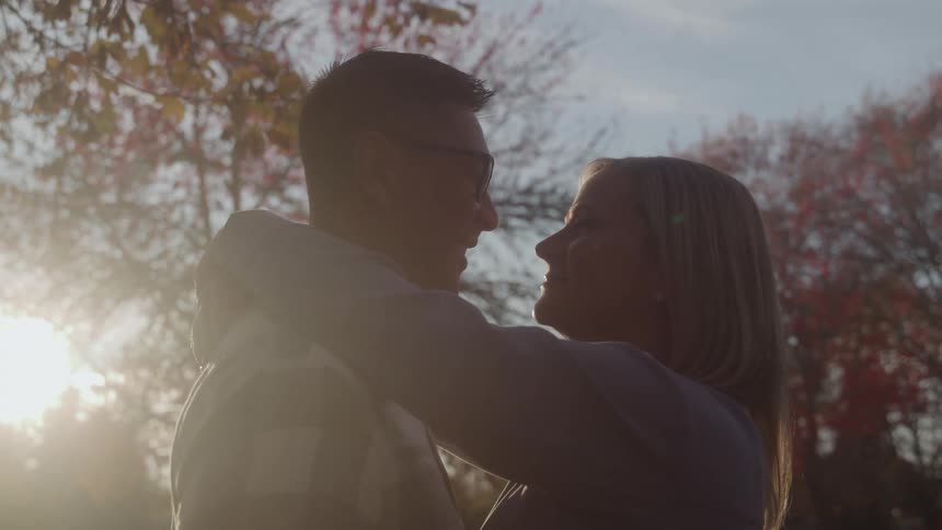 A couple embraces and gazes at each other outdoors at dusk