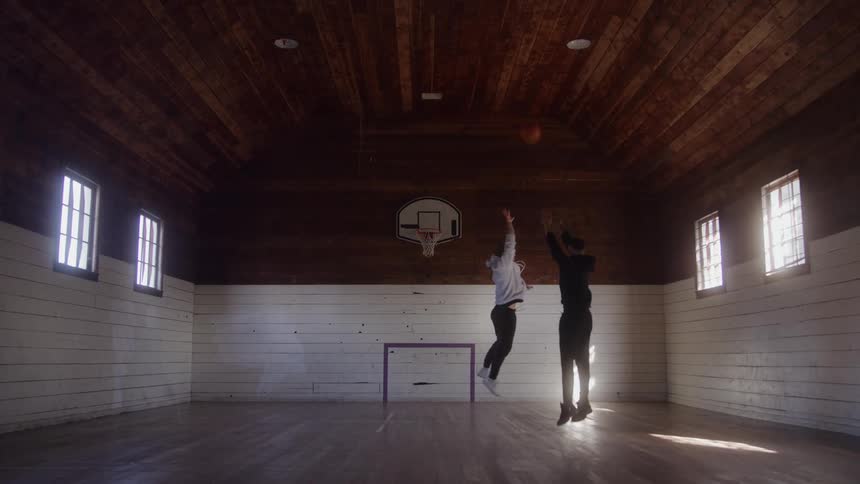 Two men play one on one basketball on an indoor basketball court during the daytime