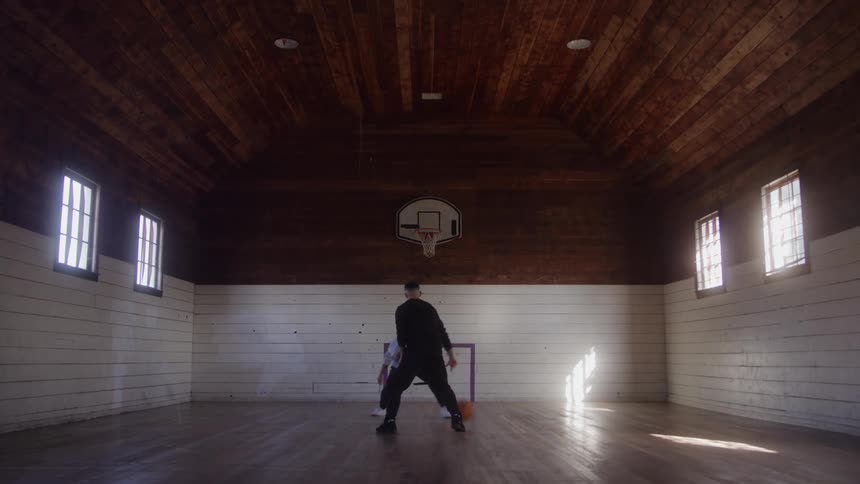 Two men face each other playing basketball in an old gymnasium