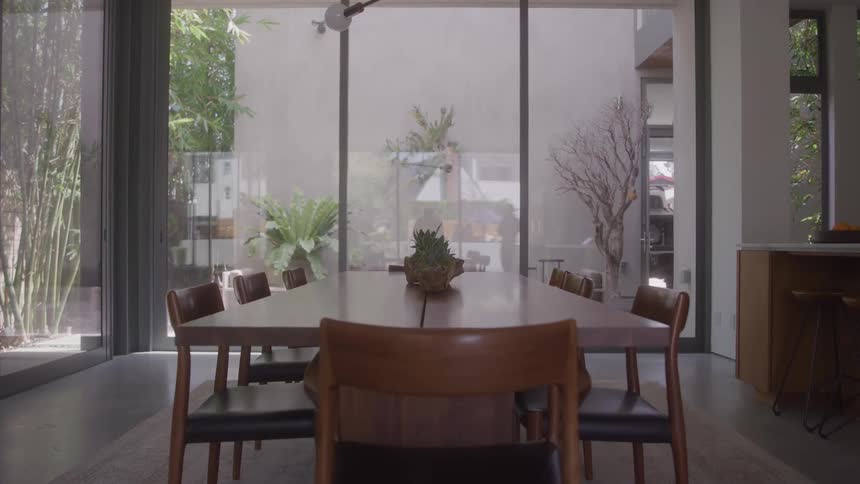 Modern wooden dining table and chairs with a lush patio visible through large windows