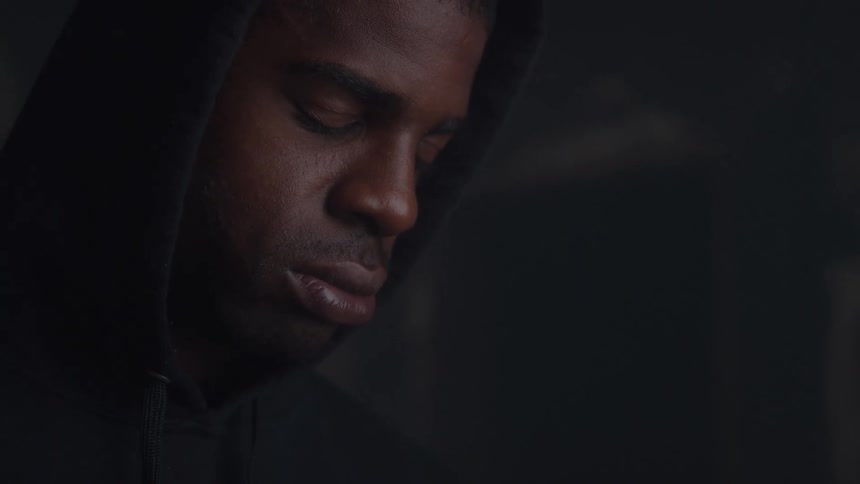 A black man wearing a blue hoodie looks down depressed