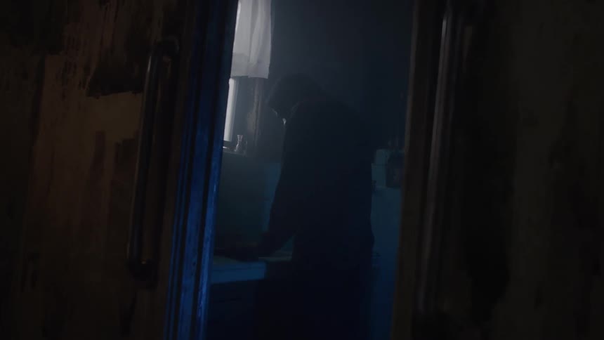 Man stands in a dimly lit dirty bathroom that has a doorway bracketed by handlebars