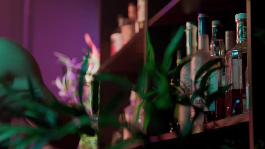 A closeup of a hand reaching for a bottle on a dimly lit bar shelf