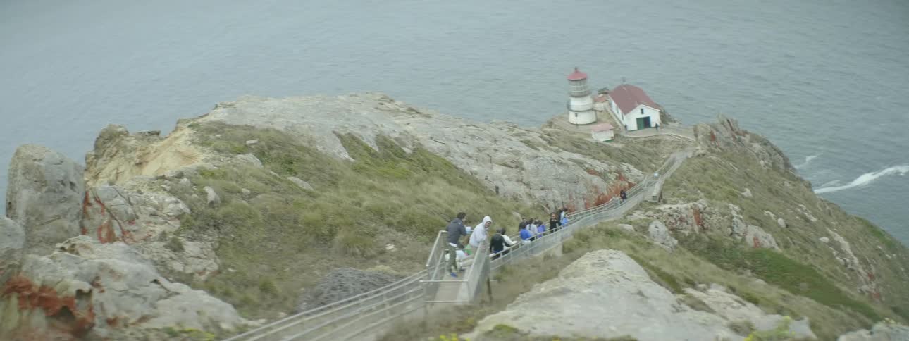 People walk down a long walkway to get to a lighthouse
