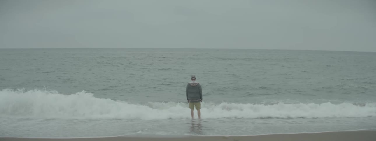 A man is standing in the waves of a beach