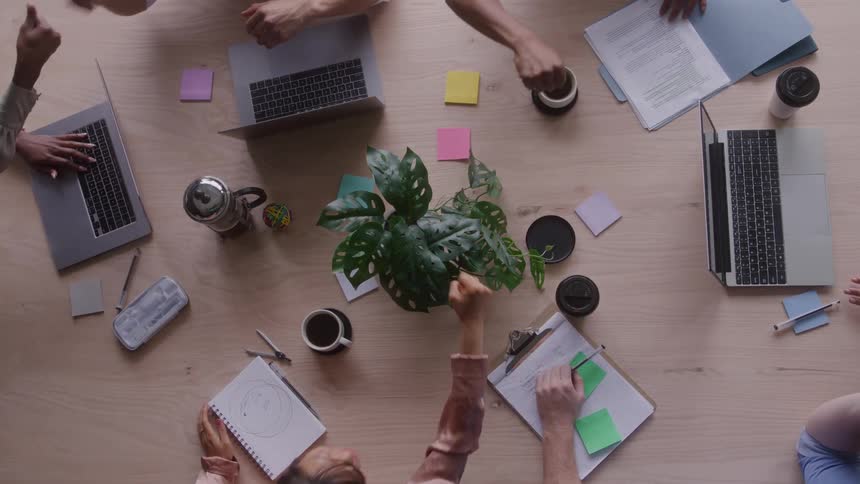 A group fist bumps over an office table with laptops and coffee