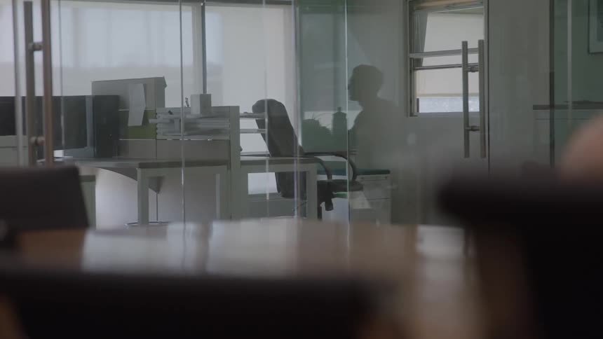 The man is sitting at the desk in the office down the hall