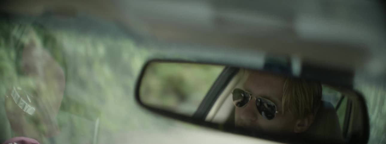 A man's reflection is shown in the rearview mirror of a moving car