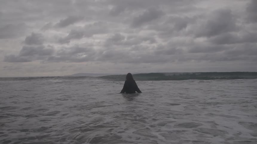 The woman stands knee high in the ocean on the beach