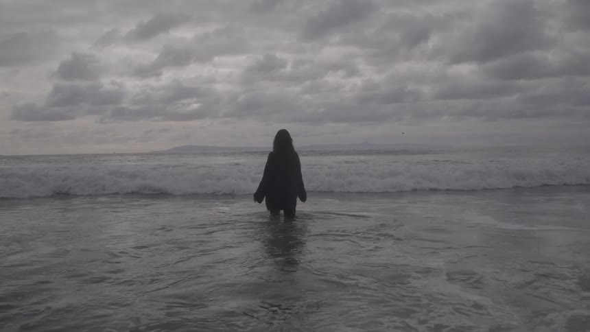 Person walking toward the crashing waves under a moody overcast sky