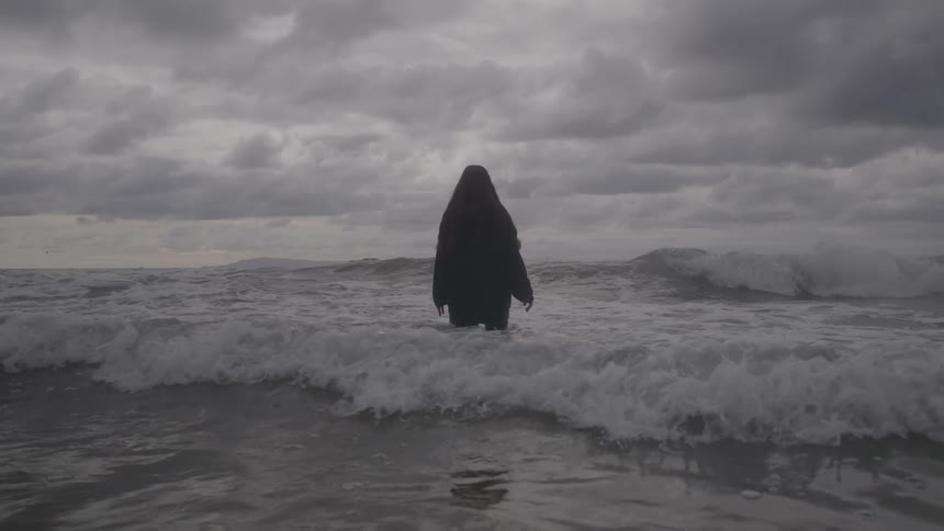 Woman standing in the water near the beach jumps into an incoming wave