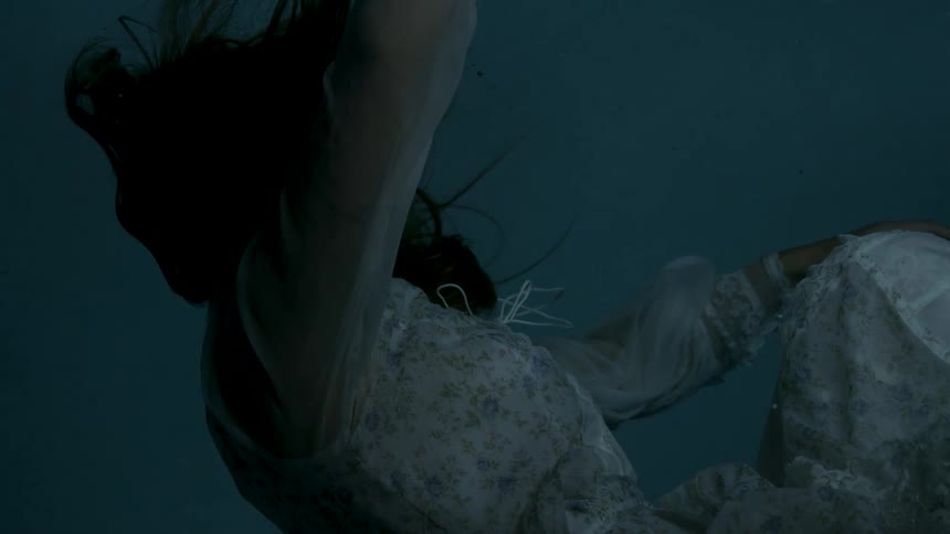 A woman floats underwater in a flowing dress beneath the surface