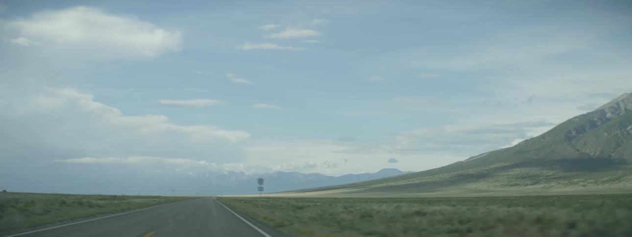 A vehicle drives on a road heading towards mountains