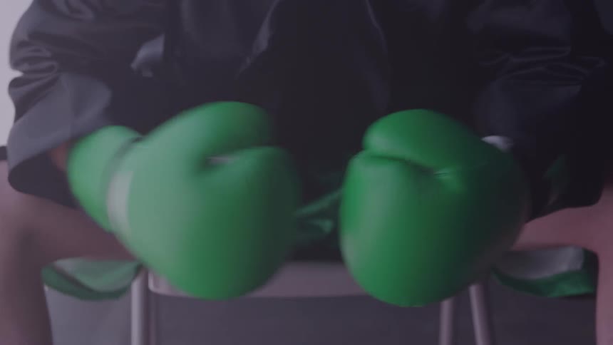 Boxer sitting on a stool taps his green boxing gloves together