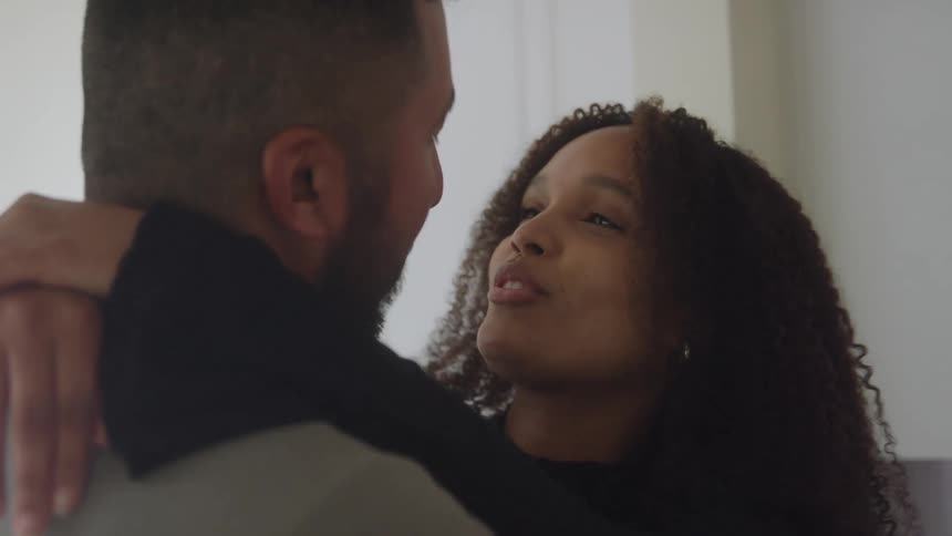 A couple smiles warmly at each other while embracing indoors