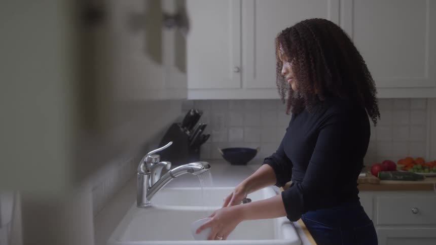 Woman stands at the kitchen sink and washes dishes