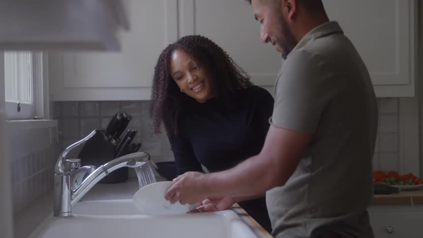 A couple affectionately washes dishes together at a kitchen sink