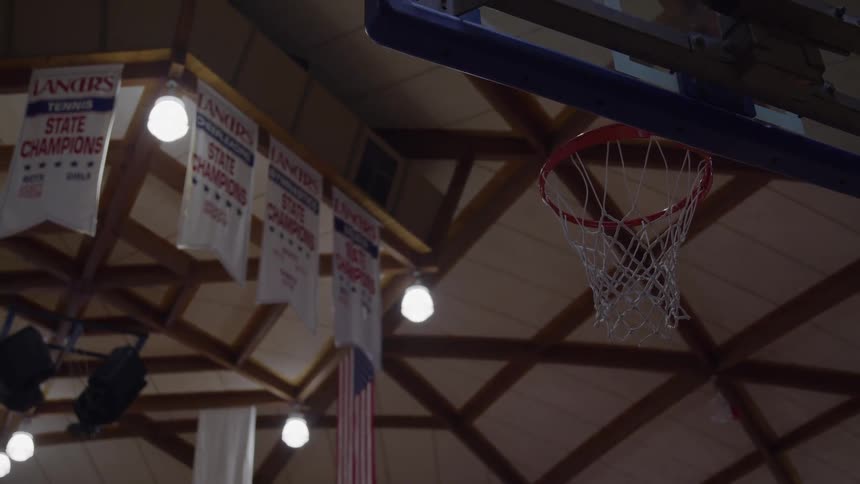 A basketball court with a basketball hoop and on the ceiling there are some banners