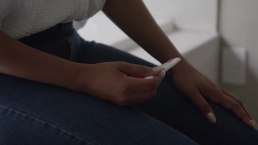 A woman sitting alone holds a pregnancy test in her hand