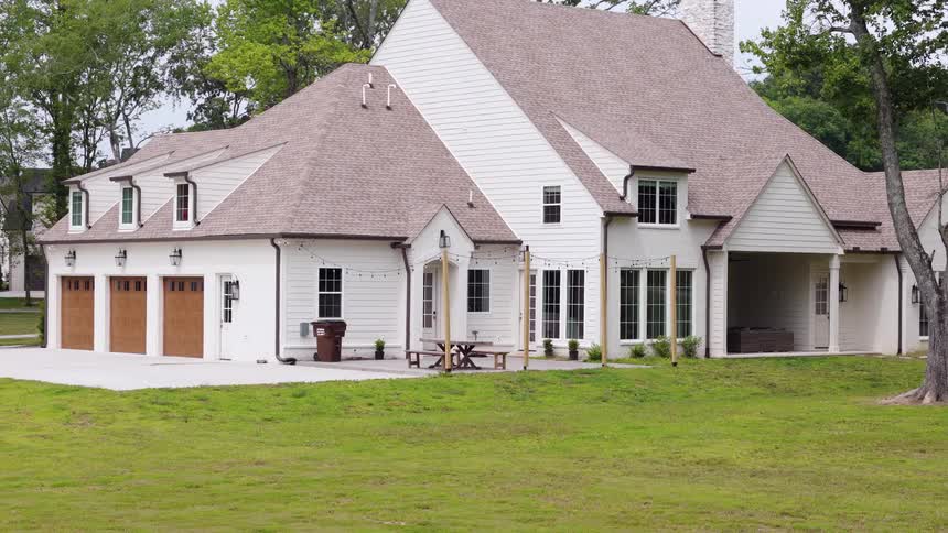 Wide exterior of a white farmhouse with a large lawn and patio
