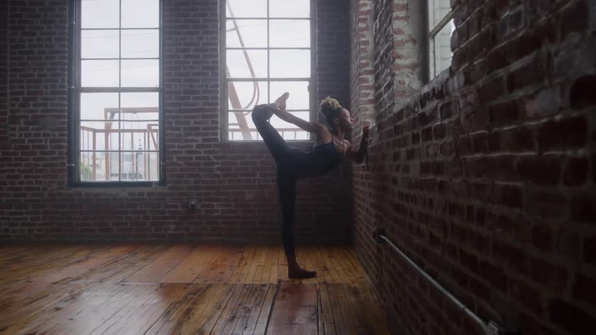 A young woman leaning against a wall and stretching her leg