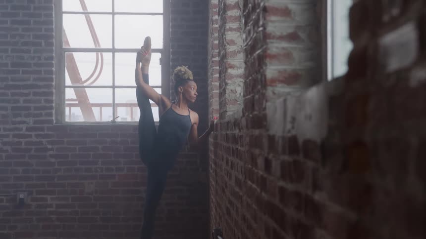 The woman does ballet while looking out the window