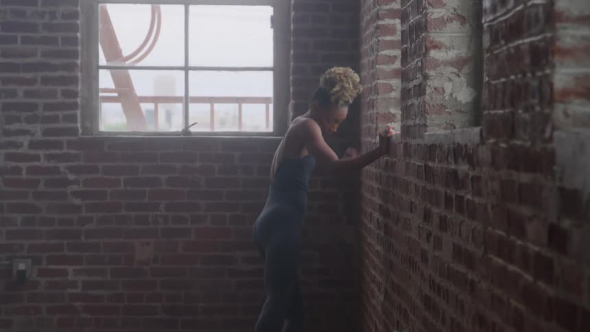 A woman dancing ballet holding onto a wall with one hand