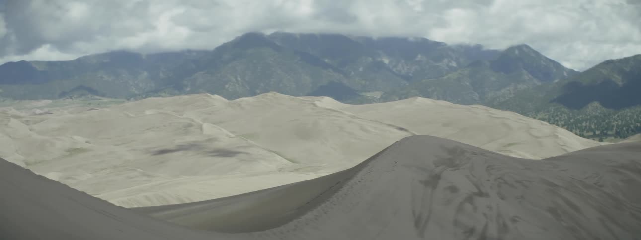 Sand dunes in front of green mountains on cloudy day