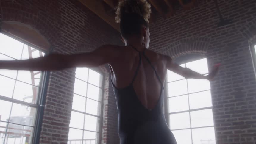 A woman is dancing ballet in a room with many windows