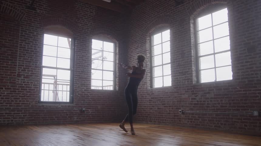 Ballerina rehearsing alone in a brick studio with tall windows