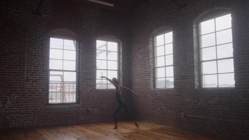 A female dancer practices alone in a dance studio with hardwood flooring