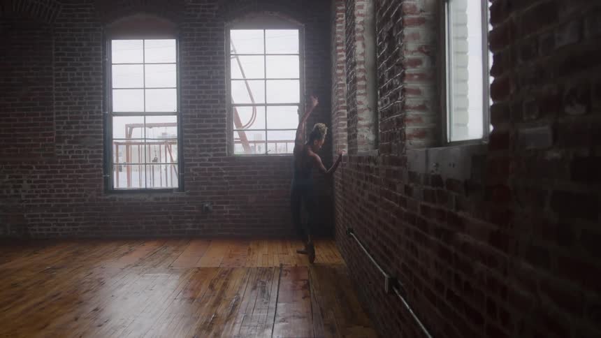 A female dancer holds onto a window ledge while practicing a dance