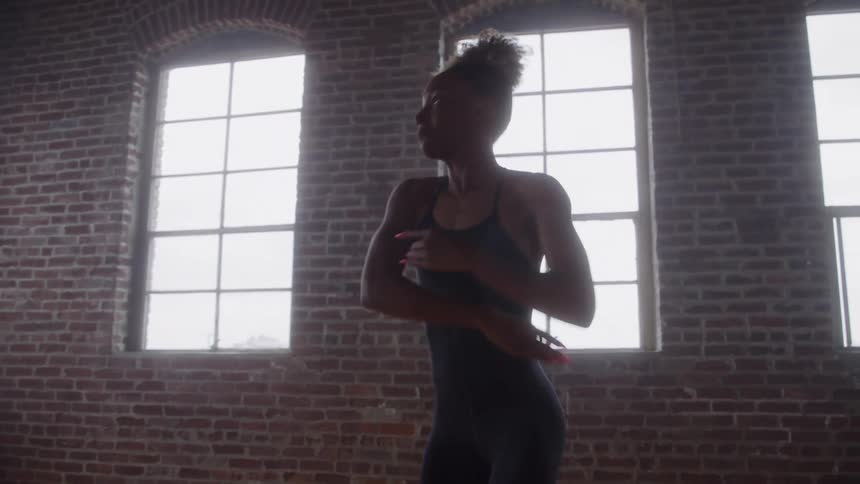 A young female ballet dancer practices alone at midday spinning gracefully in an open room with multiple windows