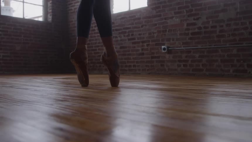 Ballerinas feet hold pointe position on wooden floor in studio with brick wall