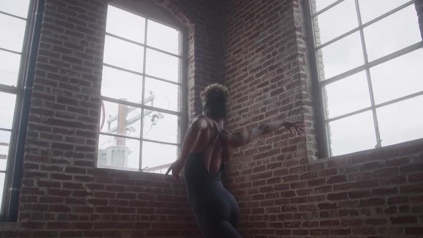 Dancer practicing graceful movements in front of large windows in a brick studio