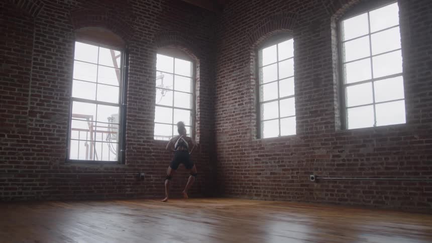 A female dancer rehearses in a dance studio with wooden floors