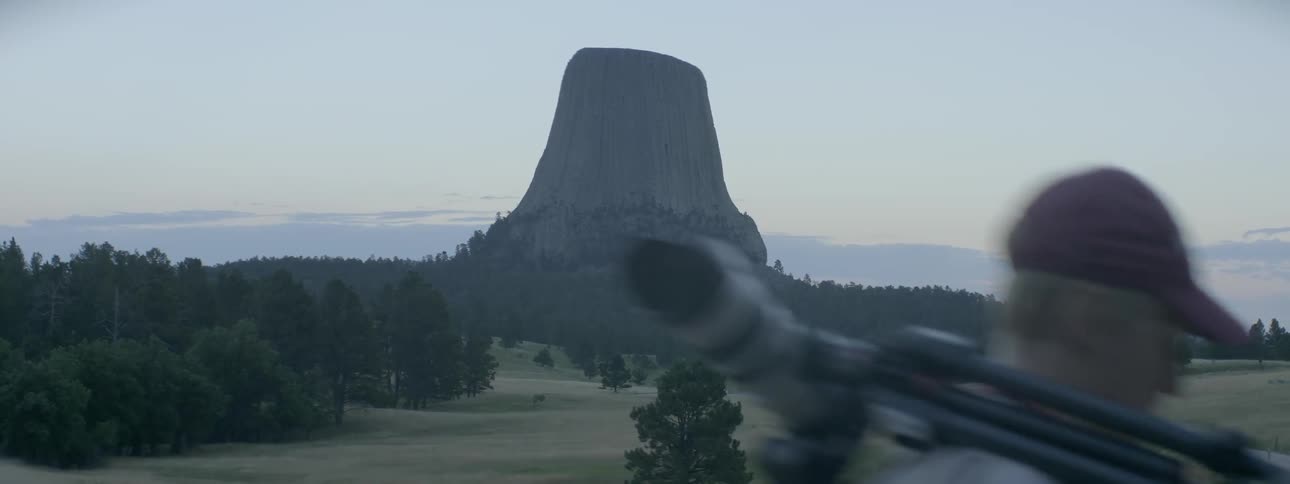 A man with a tripod and camera walks by with a large rock formation in the distance