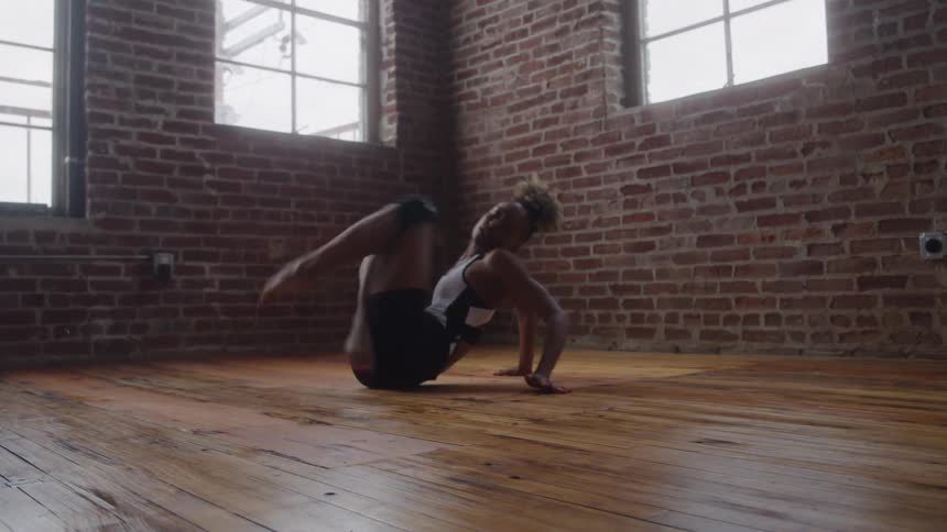 A woman practices a contemporary dance moves in a sunlit brick studio
