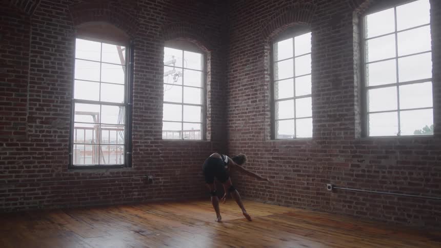 A lone female dance practices in a studio with wooden floors